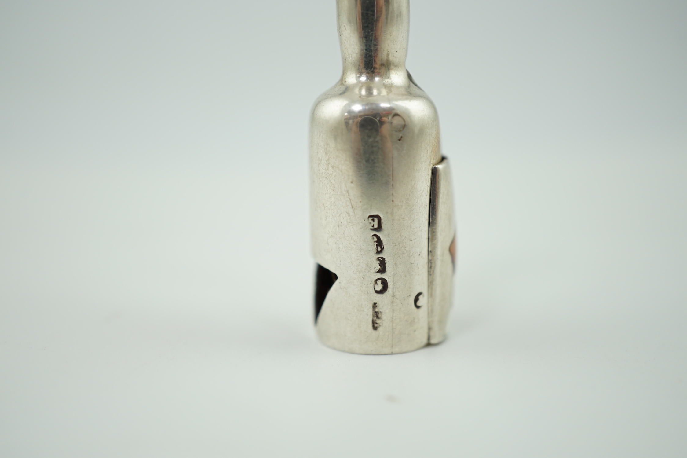 A late Victorian novelty parcel gilt silver cigar cutter, modelled as a bottle, the hinged section enamelled with a head of a dog